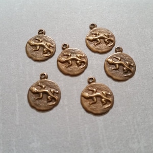 May include: Seven gold-toned metal charms featuring a lizard design. Each charm is round and has a loop at the top for attaching to a necklace or bracelet.