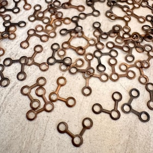 May include: A close-up of a pile of small, copper-colored metal connectors. The connectors are shaped like a Y with three circles at the ends of each arm.