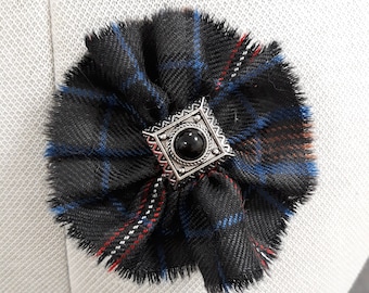 May include: A black, blue, and red plaid fabric flower with a silver and black button in the center.