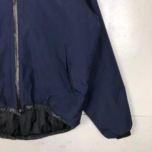 Puede incluir: Chaqueta azul marino con cremallera completa y forro negro. La chaqueta tiene un bolsillo en la parte delantera y ribetes negros en los pu&ntilde;os y el dobladillo. Fabricada con un material liso, posiblemente resistente al agua.