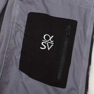 May include: Close-up of a gray jacket interior with a black pocket. The pocket features a white logo and a black zipper. The jacket's interior is a light gray color.