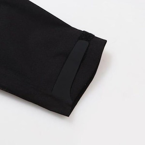 May include: Close-up of a black garment sleeve with a rectangular black patch and a small velcro closure. The sleeve is made of a smooth, dark fabric. The background is plain white.