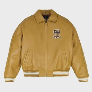 May include: Mustard yellow leather bomber jacket with a zip closure, collar, and ribbed cuffs and hem. Features a patch on the chest with the text "AVIREX" and a patriotic design. The jacket has two front pockets and a classic bomber silhouette.
