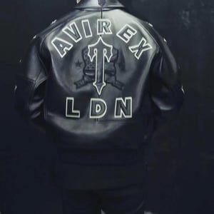 May include: Black leather jacket with white lettering on the back. The jacket features the words "AVIREX" and "LDN", along with a graphic. The jacket has a ribbed hem and cuffs.