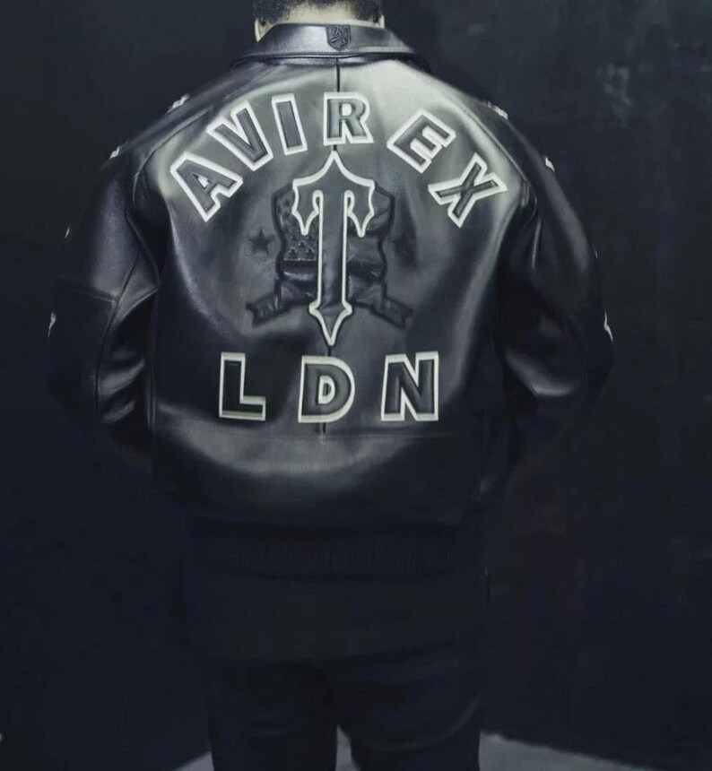 May include: Black leather jacket with white lettering on the back. The jacket features the words "AVIREX" and "LDN", along with a graphic. The jacket has a ribbed hem and cuffs.
