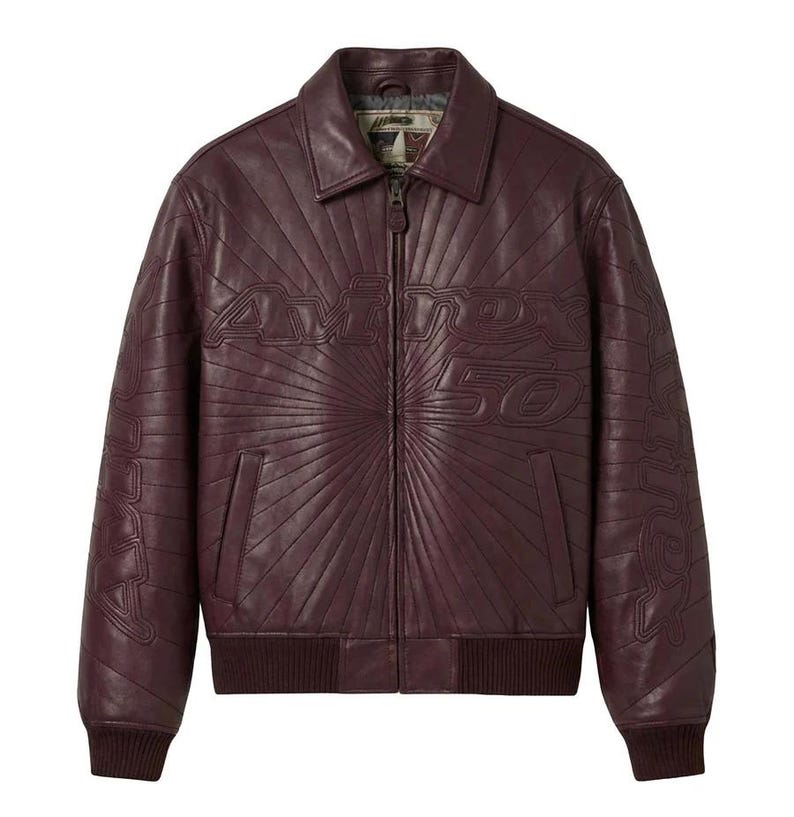 K&ouml;nnte beinhalten: Burgunderfarbene Lederjacke im Bomber-Stil. Die Jacke hat einen Rei&szlig;verschluss, einen Kragen und gerippte B&uuml;ndchen und Saum. Auf der Vorderseite der Jacke ist der Text "Avirex 50" in einem radialen Muster gepr&auml;gt.
