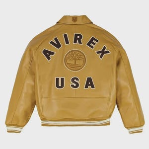 May include: Mustard-colored leather jacket with the word "AVIREX" arched across the back in brown lettering. Below the word "AVIREX" is a circular emblem and the word "USA". The jacket has a collar, ribbed cuffs, and a white stripe.