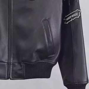 May include: Black leather jacket with white embroidered details on the sleeves and a patch on the chest. The patch reads "NY ESTABLISHED NY 1975". The jacket has a ribbed hem and cuffs.