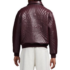 K&ouml;nnte beinhalten: Burgunderfarbene Leder-Bomberjacke mit gesteppter R&uuml;ckenpartie. Auf der R&uuml;ckseite befindet sich ein gepr&auml;gtes Design mit dem Text "AVIREX 50 GOLD KICKOFF NY". Die Jacke hat einen gerippten Kragen, B&uuml;ndchen und Saum.