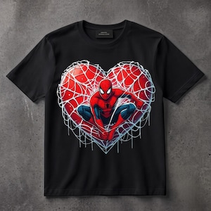 May include: A black short-sleeve t-shirt featuring a graphic print of a red heart shape filled with white spiderwebs. Centered within the heart is a red and blue superhero character in a crouching pose with large white eyes and a black spider emblem.