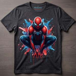 May include: A charcoal gray short-sleeve t-shirt featuring a graphic of a red and blue superhero in a crouching pose. The design includes vibrant red and blue paint splatter effects. The inner neck label reads Hero Collective Premium Slate Edition.