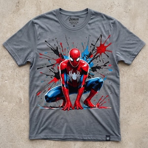 May include: A heather gray short-sleeve t-shirt featuring a graphic of Spider-Man in a crouching pose. The design includes red, blue, and black paint splatter effects. The inner neck label reads Avengers Collective, Premium Cotton, Made in USA.
