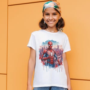 May include: A white short-sleeve t-shirt featuring a graphic print of the superhero Spider-Man in a red and blue suit, positioned in front of a stylized city skyline with watercolor-style paint drips at the bottom of the illustration.