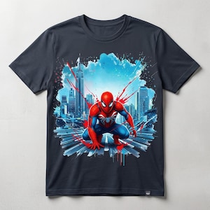 May include: A dark gray short-sleeve t-shirt featuring a graphic print of a red and blue costumed character in a crouching pose. The background displays a stylized city skyline with blue and red paint splatter effects across the chest area.