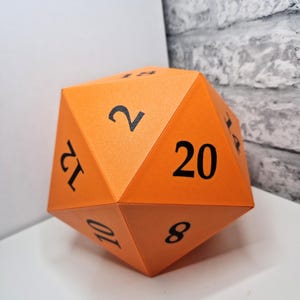 May include: An orange twenty-sided die, also known as an icosahedron, featuring bold black numbers printed on each triangular face. The visible numbers include 2, 8, 10, 12, 14, 18, and 20, clearly displayed against the matte orange surface.