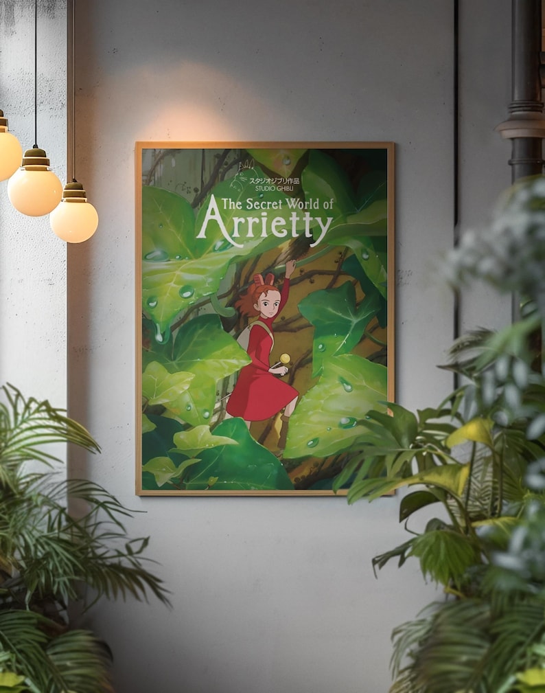 Pu&ograve; includere: Un poster incorniciato del film d'animazione "Arrietty - Il mondo segreto sotto il pavimento". L'opera raffigura una ragazza in abito rosso tra un rigoglioso fogliame verde. Il poster ha una cornice in legno ed &egrave; su un muro strutturato.