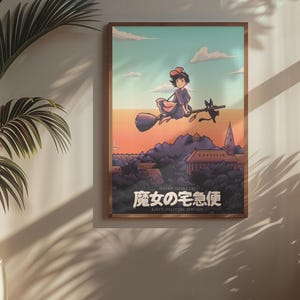 Op de afbeelding: Een ingelijste rechthoekige wandkunstprint met een geanimeerde illustratie van een personage dat op een bezemsteel met een zwarte kat door een zonsonderganglucht boven een stad vliegt. De Japanse tekst luidt 魔女の宅急便 en de Engelse tekst KIKI'S DELIVERY SERVICE.