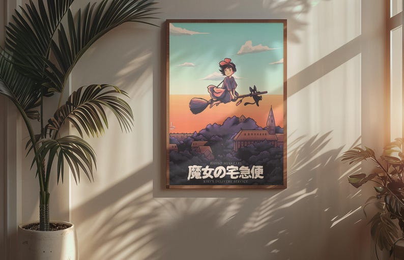 Op de afbeelding: Een ingelijste rechthoekige wandkunstprint met een geanimeerde illustratie van een personage dat op een bezemsteel met een zwarte kat door een zonsonderganglucht boven een stad vliegt. De Japanse tekst luidt 魔女の宅急便 en de Engelse tekst KIKI'S DELIVERY SERVICE.