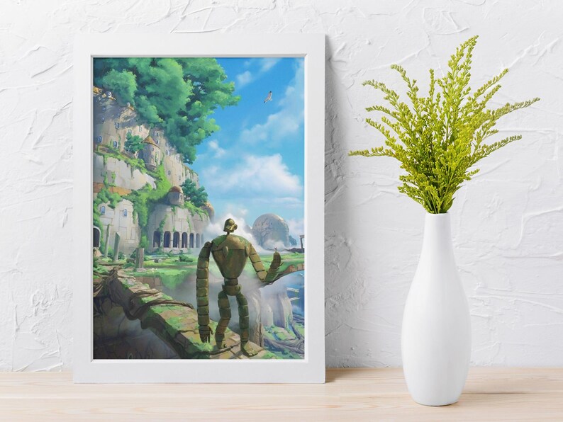 Puede incluir: Una impresi&oacute;n art&iacute;stica enmarcada que presenta una escena con una gran figura de robot que domina un paisaje con edificios y exuberante vegetaci&oacute;n. La obra de arte est&aacute; ambientada contra un cielo azul con nubes. Un jarr&oacute;n blanco con follaje verde est&aacute; a la derecha.