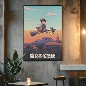 Op de afbeelding: Een rechthoekige wandposter met een geanimeerde illustratie van een jong persoon met een rode strik die op een bezemsteel vliegt met een zwarte kat. Daaronder ligt een stad met paarse heuvels en de Japanse tekst 魔女の宅急便.