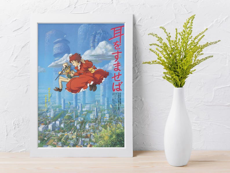 May include: A framed poster featuring anime artwork. The image depicts two characters in mid-air over a cityscape, with text in Japanese. The artwork is set against a blue sky with cloud-like structures. A white vase with green foliage is to the right.
