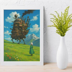 May include: A framed art print featuring a scene from the animated film "Howl's Moving Castle." The artwork depicts a large, walking castle on a grassy hill, a figure in a green dress, and a mountain range under a blue sky with clouds. The print is in a white frame.