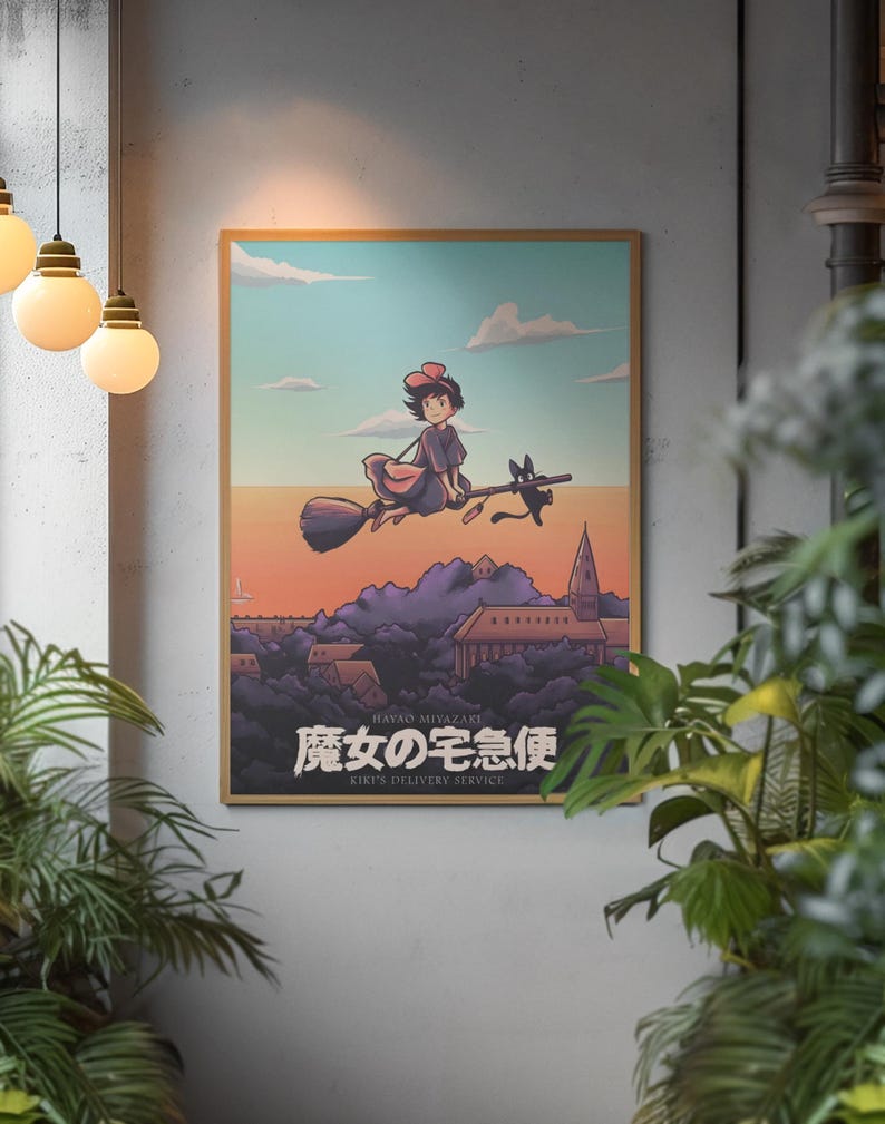 Op de afbeelding: Een ingelijste poster met een illustratie van een jong persoon met een rode strik die op een bezemsteel met een zwarte kat over een stad vliegt bij zonsondergang. De tekst bevat Hayao Miyazaki, 魔女の宅急便 en Kiki's Delivery Service in witte letters.