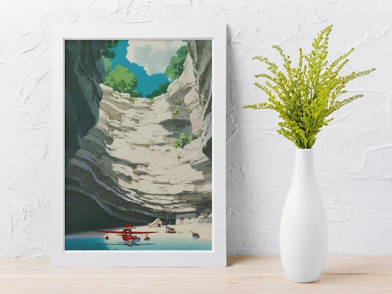May include: A framed art print depicts a canyon scene with a red airplane on a beach. The artwork features a detailed illustration of layered rock formations, a blue sky with clouds, and green foliage. A white vase with green plants is on a wooden surface.