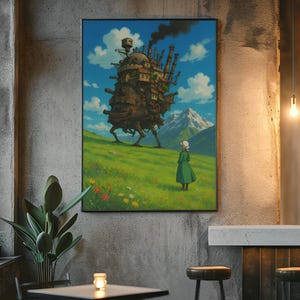 May include: A framed art print depicting a scene from an animated film. The artwork shows a walking castle on a grassy hill, a figure in a green dress, and a mountain range under a blue sky with clouds. The print is displayed on a textured gray wall.