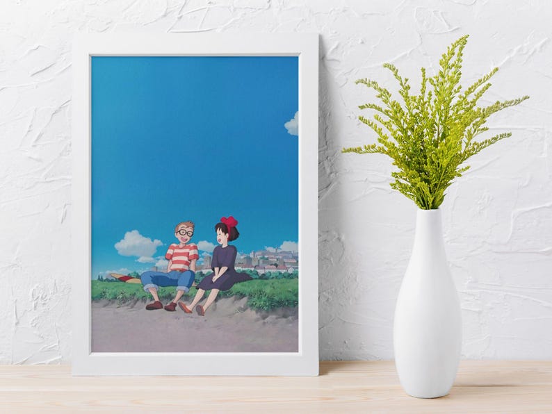 May include: A framed art print featuring an anime-style illustration of two characters sitting on a grassy hill under a bright blue sky with fluffy white clouds. One character wears a red and white striped shirt, the other a black dress.