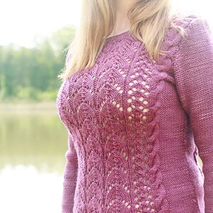 Puede incluir: Primer plano de una mujer con un suéter de punto malva con un patrón de encaje. El suéter tiene mangas largas y un escote redondo. La mujer lleva pantalones vaqueros azules.