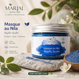 Op de afbeelding: Een pot blauw gezichtsmasker met de tekst "Masque au Nila" en "MARJAL SKINCARE" op het etiket. De pot staat op een stenen oppervlak met een houten kom met blauw poeder en witte bloemen. Natuurlijk, biologisch thema.