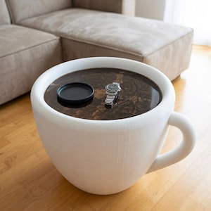 Peut inclure: Une table en forme de tasse à café blanche remplie de liquide foncé, avec une soucoupe noire et une montre-bracelet argentée. La table a une grande anse et repose sur un sol en bois. C'est un meuble unique.