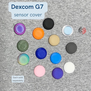 May include: A collection of circular Dexcom G7 sensor covers in various solid colors including black, orange, beige, blue, pink, purple, white, green, and iridescent finishes. The text Dexcom G7 sensor cover and Each sold separately are visible.