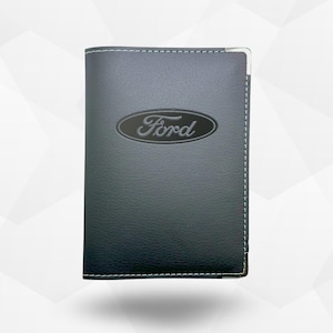 Puede incluir: Una cartera de cuero negro con el logotipo de Ford en relieve en la parte delantera. La cartera tiene costuras blancas alrededor de los bordes y una esquina de metal plateado. El logotipo de Ford está en un óvalo plateado.