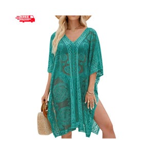 May include: A teal green sheer lace cover-up featuring a V-neckline, short wide sleeves, and an intricate floral pattern throughout. The garment has a loose, flowing silhouette with side slits and is paired with a woven straw handbag.