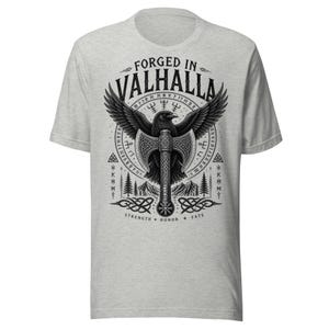 May include: Pale grey t-shirt with a black and white graphic of an eagle, axe, and the words "FORGED IN VALHALLA". The design also includes the words "STRENGTH HONOR FATE" in a circular pattern.