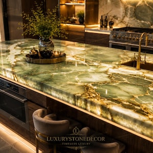 May include: A luxurious kitchen countertop made of green and gold veined stone. A decorative vase with greenery sits on the countertop, along with a tray holding candles and a decorative container. A stainless steel oven is visible.