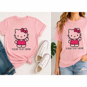 Pode incluir: Duas camisetas rosa com um desenho de gato de desenho animado com um la&ccedil;o rosa e o texto "YOUR TEXT HERE". T&ecirc;nis brancos e jeans azuis tamb&eacute;m s&atilde;o vis&iacute;veis.