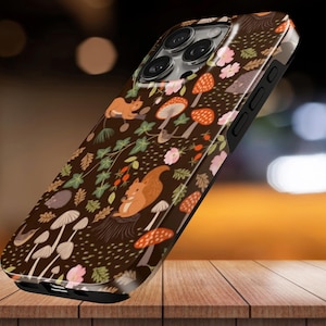 May include: A smartphone case featuring a dark brown background with a repeating pattern of orange squirrels, various white and orange mushrooms, pink flowers, green leaves, and small brown acorns scattered across the entire surface area.