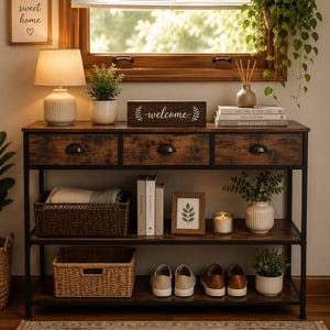 May include: A rectangular console table with a dark wood grain finish and a black metal frame. It features three top drawers with black cup pulls and two lower shelves holding woven baskets, books, a framed leaf print, a candle, and shoes.