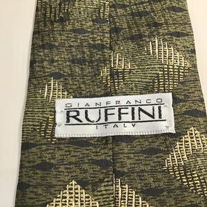 May include: An olive green necktie featuring a repeating pattern of dark horizontal lines and light yellow diamond shapes. A white fabric label is stitched onto the center, displaying the black text GIANFRANCO RUFFINI ITALY in a clear font.