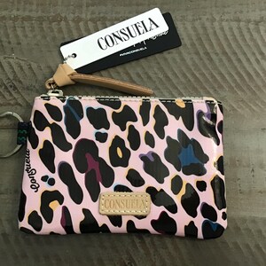 May include: A rectangular zippered pouch featuring a pink, black, and blue leopard print pattern. The pouch includes a silver metal key ring on the side, a tan leather-like zipper pull, and a tan patch with the text CONSUELA. A white tag with the text CONSUELA is attached.