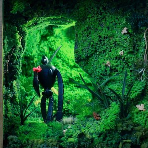 May include: A black robot figure holding a red flower stands in a lush, green mossy environment. The scene is illuminated with a bright green light, creating a whimsical and fantastical atmosphere. The robot has a sleek, minimalist design.