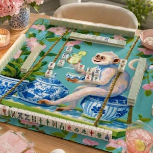 May include: A Mahjong set featuring a game board with a light blue background, pink floral patterns, and a central illustration of a monkey sitting on a blue and white porcelain jar. The board includes rows of tiles and a matching set of game pieces.