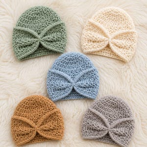 May include: Five crochet hats arranged in a cluster, each featuring a central knotted bow detail. The hats are coloured in sage green, cream, light blue, mustard yellow, and grey. Each piece is crafted with a consistent textured stitch pattern.
