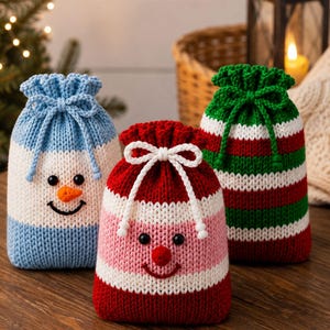 May include: Three knitted drawstring pouches featuring holiday designs. One is light blue and white with a snowman face, one is red, white, and pink with a face, and one has red, white, and green horizontal stripes with a green drawstring.