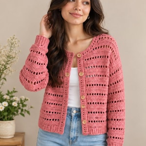 May include: A dusty rose crochet cardigan featuring a round neckline, long sleeves, and a button-down front with five light brown wooden buttons. The garment is crafted with a repeating pattern of solid horizontal rows and openwork vertical stripes.