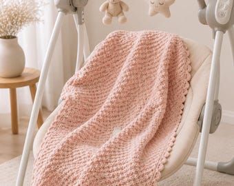 May include: A light pink crocheted baby blanket with a scalloped edge draped over a beige infant swing. The swing features a gray arched toy bar with a hanging plush beige teddy bear and a plush cream-colored star with a stitched sleeping face.