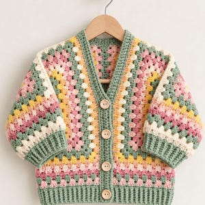 Peut inclure: Un gilet à col en V composé de carrés granny au crochet dans des tons vert sauge, rose tendre, crème et jaune pâle. Le vêtement présente des manches trois-quarts, un ourlet et des poignets côtelés vert sauge, et quatre boutons en bois clair.